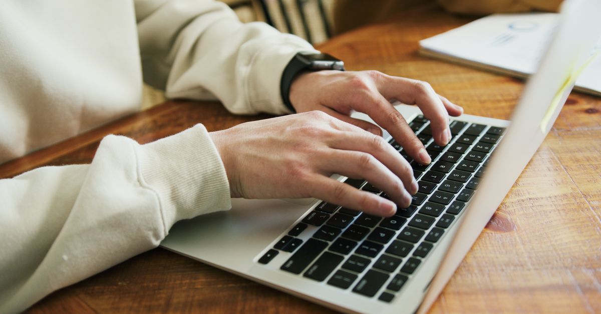 Manos escribiendo sobre el teclado de un portátil en un escritorio con poca luz