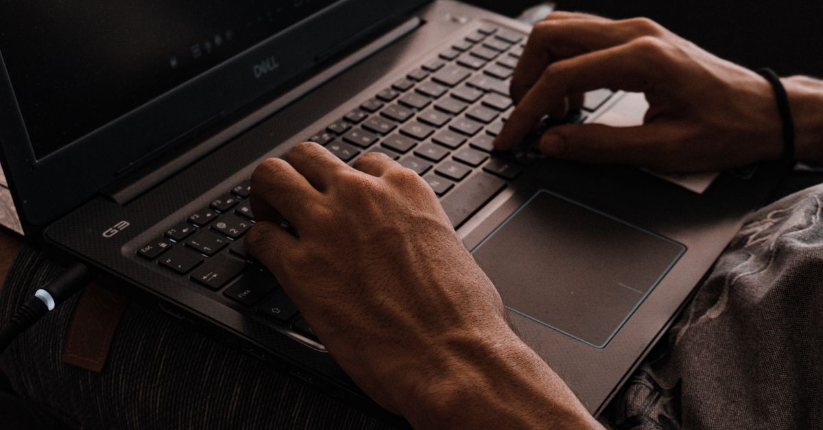 Manos escribiendo sobre el teclado de un portátil en un escritorio con poca luz